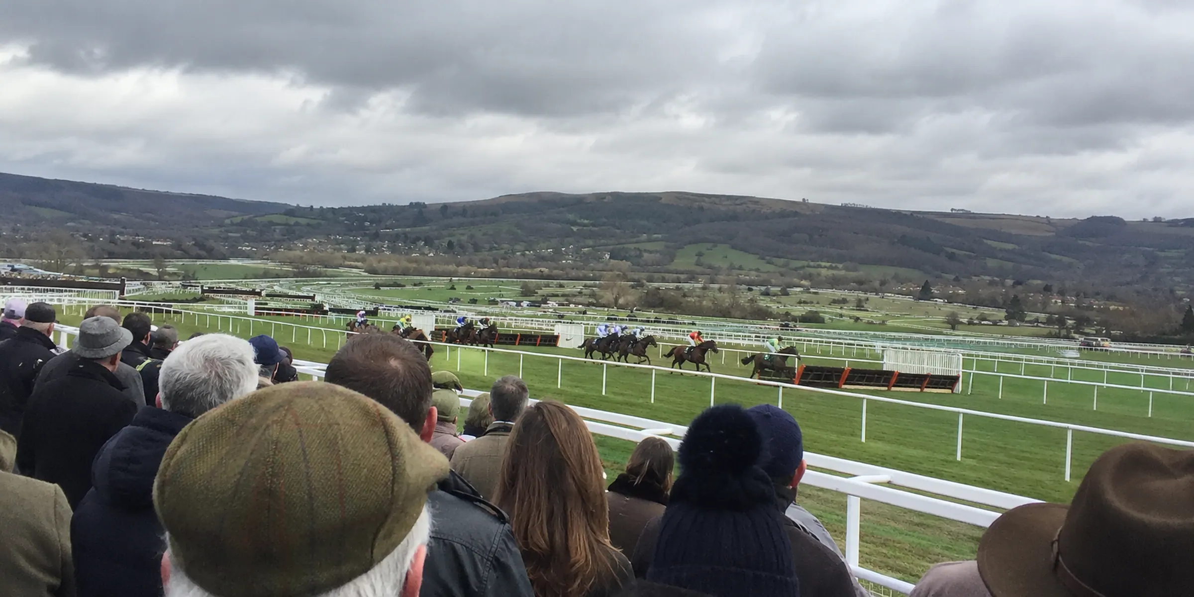 Spectators seen from behind watching jumps horses with hills beyond