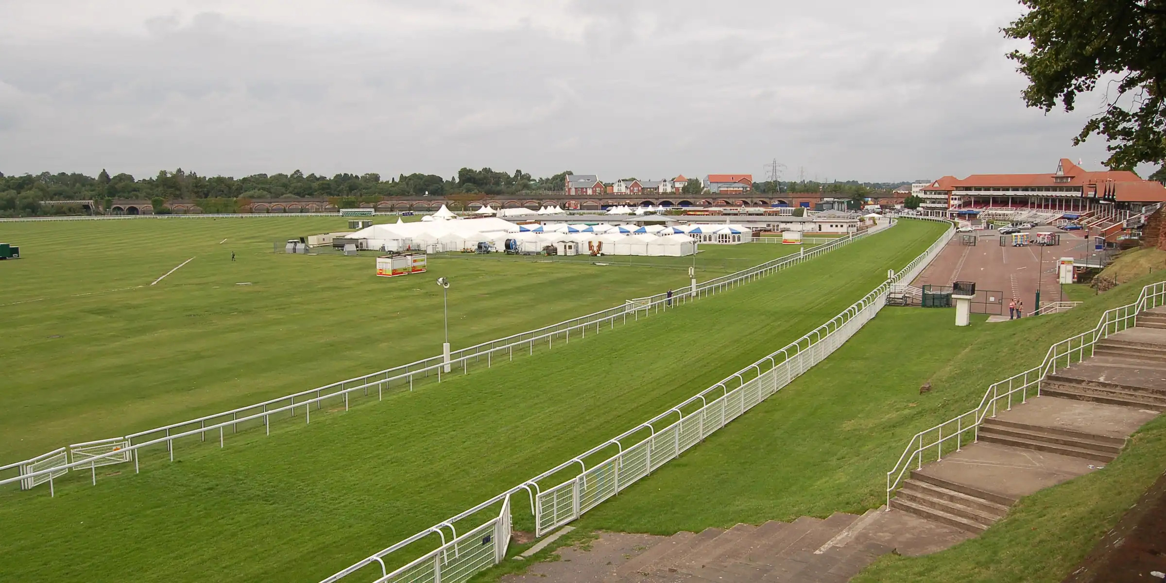 A wide view over Chester racecourse with white rails and distant stands