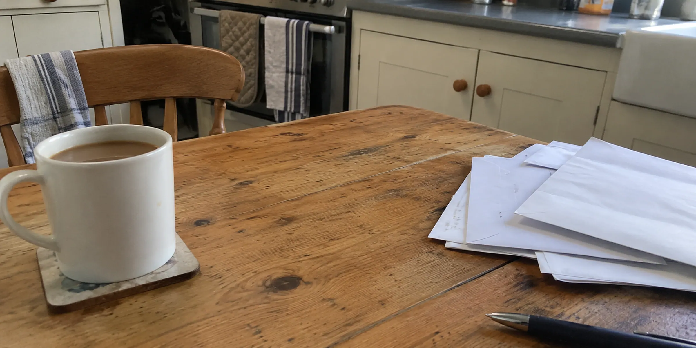 A loose pile of face-down envelopes and papers beside a mug on a kitchen table