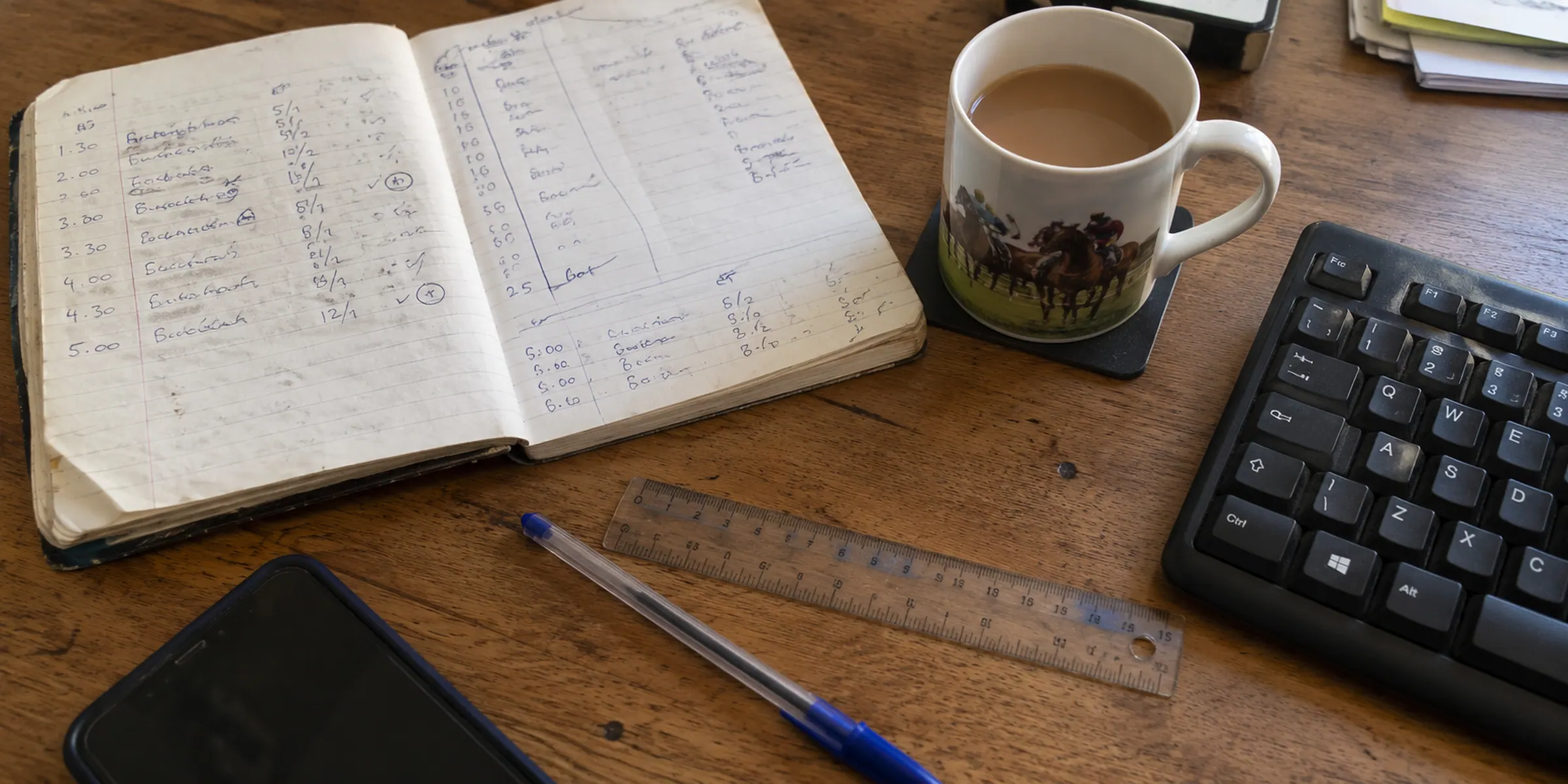 A handwritten notebook, ruler and pen on a desk beside a keyboard