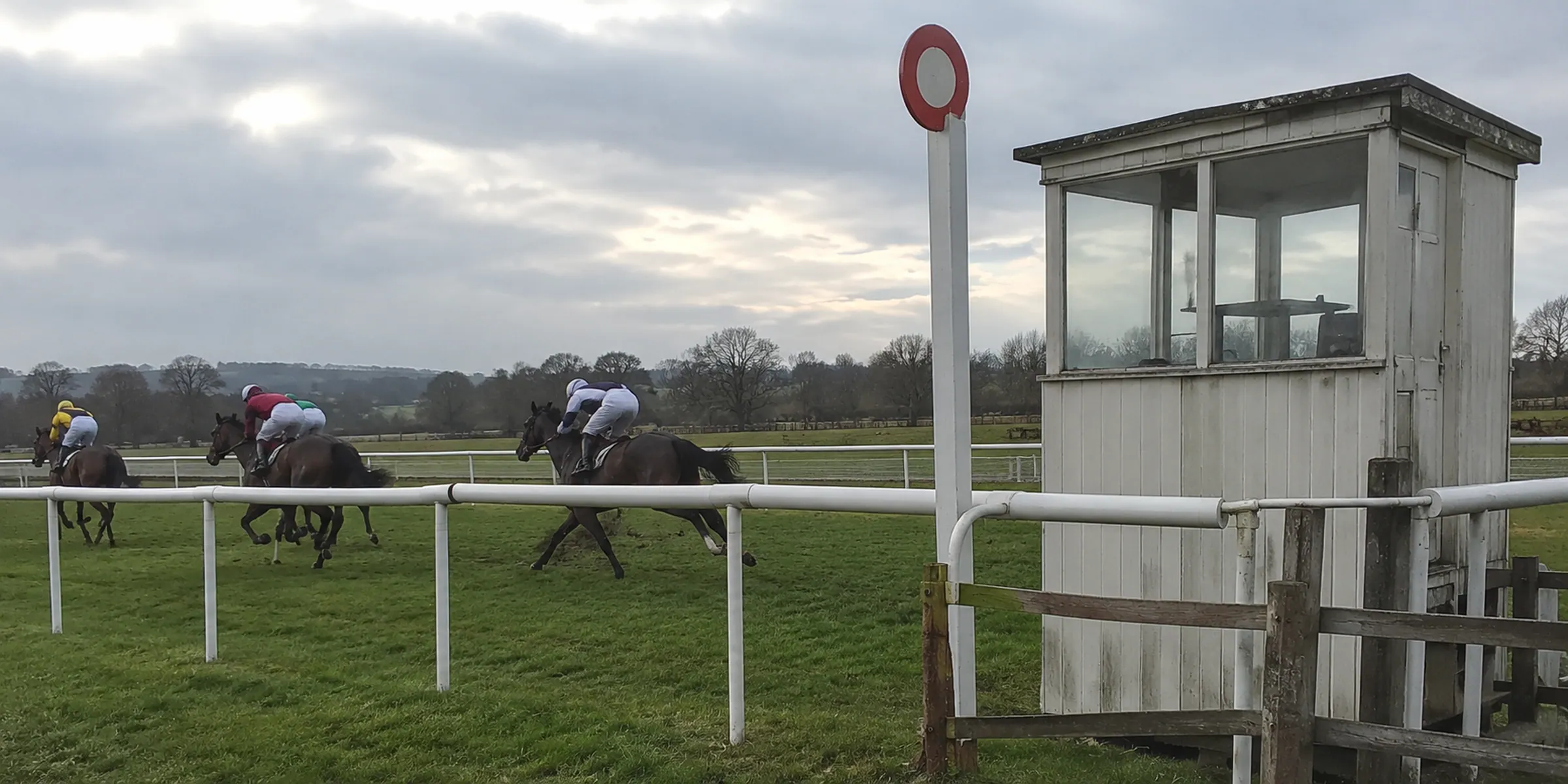 A weathered judge’s booth beside a finishing post and passing horses